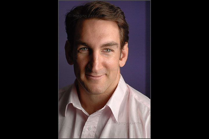 Profile portrait of Jason Urbanowicz in a light pink shirt, set against a purple background.