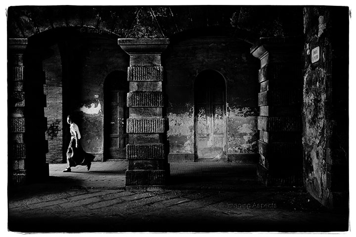 A woman with flowing dress walks through Porta S. Pietro (Saint Pietro Gate) in Lucca, Italy.