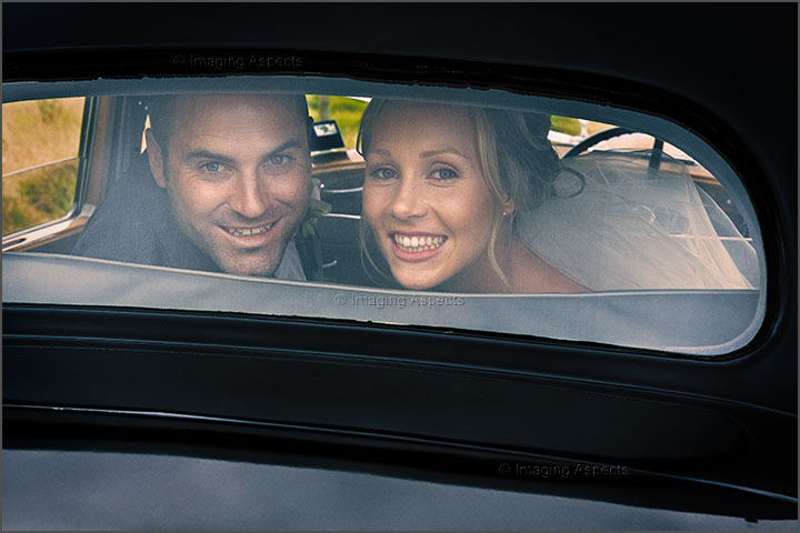 Newlyweds smile at the camera through the rear window of their Bentleigh Limousine.